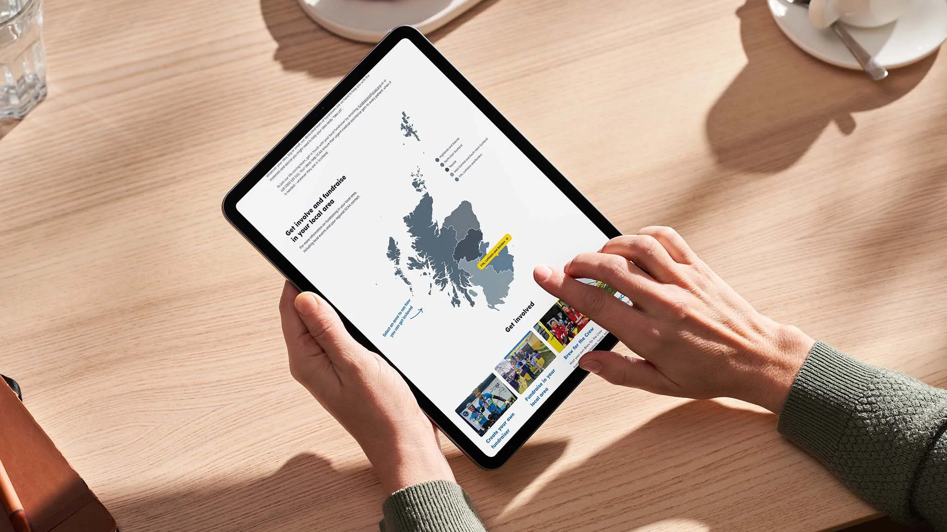 A person using a tablet to view Scotland’s Charity Air Ambulance’s website, showing an interactive map of Scotland and fundraising opportunities.