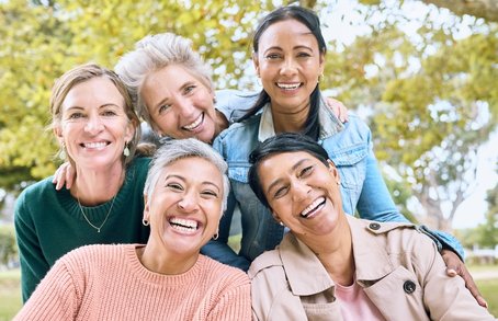 A group of five diverse, smiling women enjoying time together outdoors, symbolising community, empowerment, and the shared goal of breast cancer prevention.