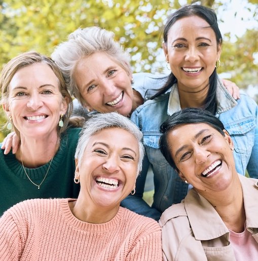 A group of five diverse, smiling women enjoying time together outdoors, symbolising community, empowerment, and the shared goal of breast cancer prevention.