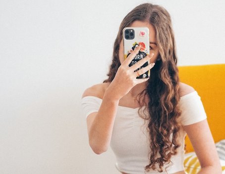 Young woman in a white top takes a selfie with a decorated phone, representing a social media influencer.