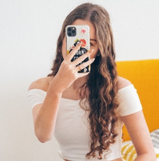 Young woman in a white top takes a selfie with a decorated phone, representing a social media influencer.