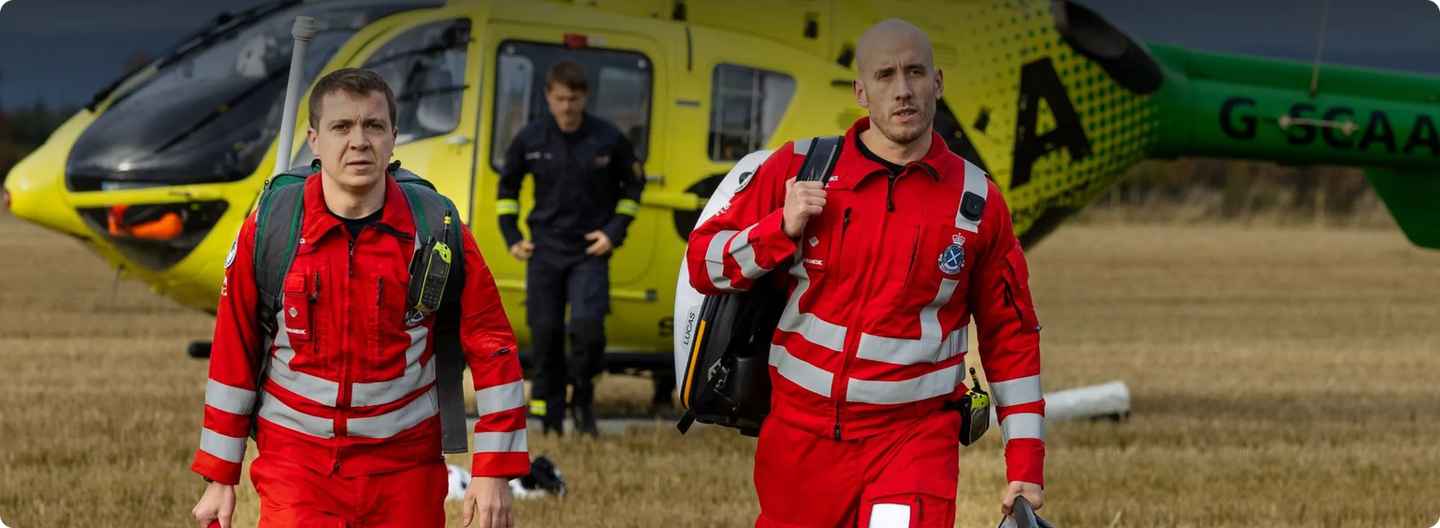 Two Scotland’s Charity Air Ambulance crew members in red uniforms walking from a yellow helicopter, used as a small case study image.