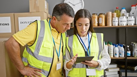 Two charity workers using a tablet to explore AI-powered tools for streamlining donation management and improving operational processes in a community support setting.