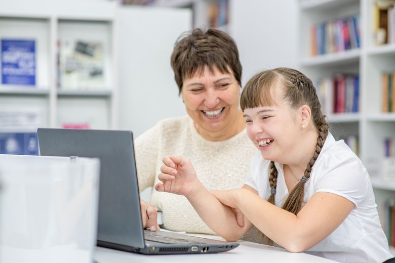 an adult and young girl with disabilities looking at a computer screen, laughing