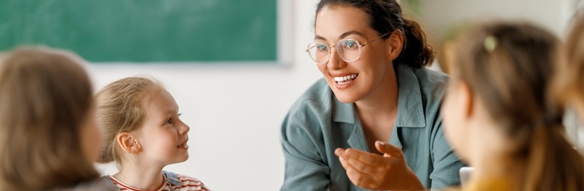 A smiling teacher engages with a group of young children in a classroom, creating a warm, inclusive learning environment — reflecting the spirit of support and empowerment in SEND education.