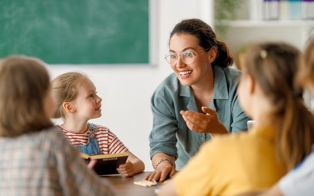 A smiling teacher engages with a group of young children in a classroom, creating a warm, inclusive learning environment — reflecting the spirit of support and empowerment in SEND education.