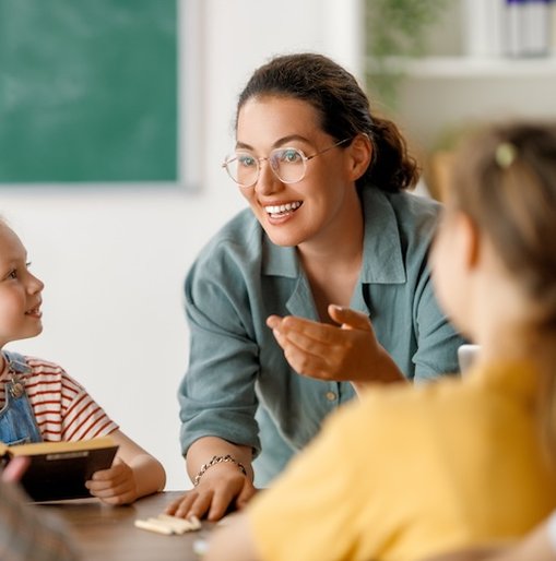 A smiling teacher engages with a group of young children in a classroom, creating a warm, inclusive learning environment — reflecting the spirit of support and empowerment in SEND education.