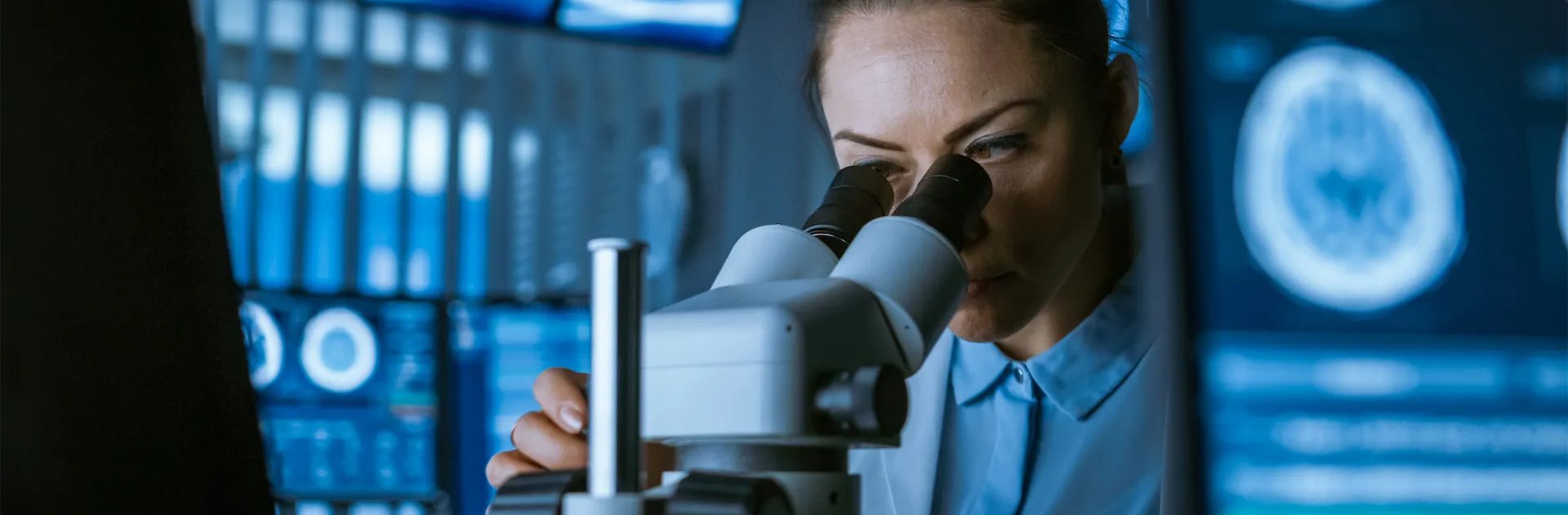 A scientist closely examining samples through a microscope in a high-tech lab, with medical imaging scans visible in the background, representing cutting-edge, evidence-based breast cancer prevention research.