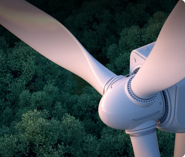 A close-up view of a wind turbine rotor and blades seen from above, with a dense forest canopy visible below.