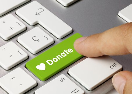 Close-up of a finger pressing a green keyboard key labelled “Donate” with a white heart icon, symbolising online giving.