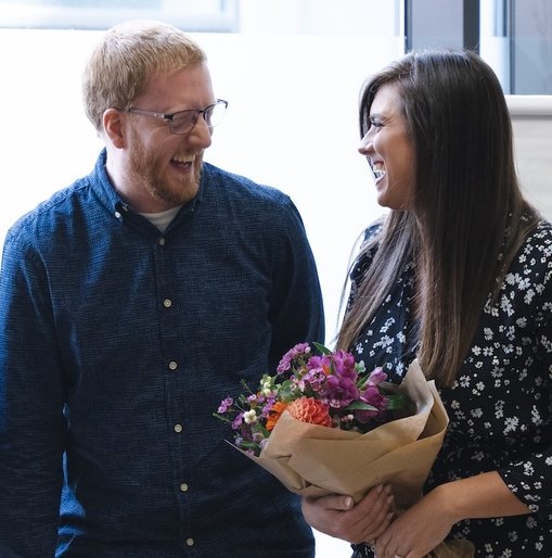 Three Giant Digital colleagues smiling and celebrating together in a bright office space. One person holds a bouquet of flowers, while another claps in appreciation.