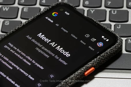 A smartphone screen displaying Google's AI Mode interface with the headline "Meet AI Mode" and example prompts, placed on top of a laptop keyboard.
