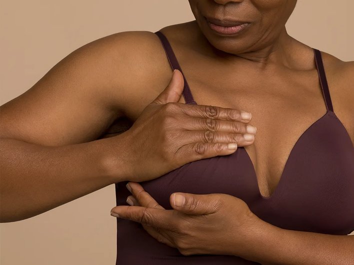A woman in a maroon bra carrying out a breast self-examination, with hands positioned on her breast.