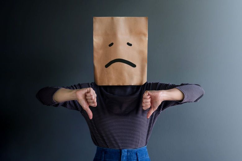 Woman Covering her Face with a Paper Bag that has a sad face drawn on it