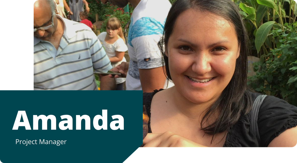 Amanda, smiling in a black top, holds out her hand with a butterfly resting on it, surrounded by greenery and a crowd of people.