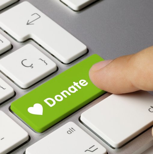 Close-up of a finger pressing a green keyboard key labelled “Donate” with a white heart icon, symbolising online giving.